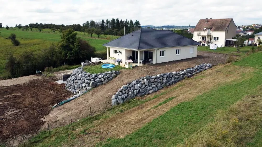 Chantier de construction résidentielle avec maison individuelle neuve à toit gris, murs blancs et terrasse couverte